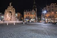 an old cobblestone plaza at night with two statues and a statue in the background