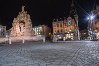 an old cobblestone plaza at night with two statues and a statue in the background