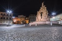 an old cobblestone plaza at night with two statues and a statue in the background