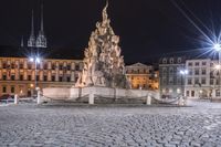 an old cobblestone plaza at night with two statues and a statue in the background