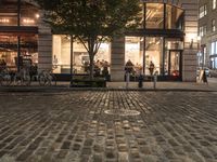 a brick street with tables, benches and trees in front of it at night time
