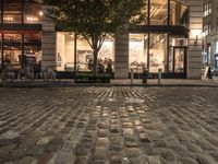 a brick street with tables, benches and trees in front of it at night time