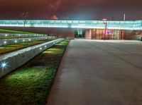 concrete benches at night with a lighted walkway leading to a building and a green lawn