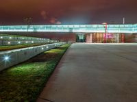 concrete benches at night with a lighted walkway leading to a building and a green lawn