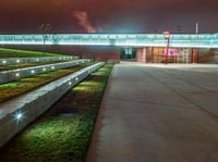 concrete benches at night with a lighted walkway leading to a building and a green lawn