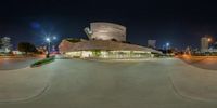 a large modern building with multiple floors and a circular roof at night time with the city's lights on