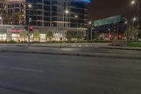 an empty street with stores and lights at night time outside of a building in downtown