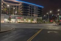 an empty street with stores and lights at night time outside of a building in downtown