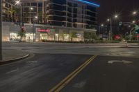 an empty street with stores and lights at night time outside of a building in downtown