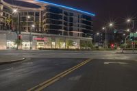 an empty street with stores and lights at night time outside of a building in downtown