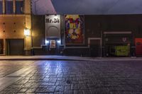 an empty brick street at night with posters on the side of it in the dark