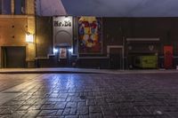 an empty brick street at night with posters on the side of it in the dark