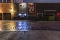 an empty brick street at night with posters on the side of it in the dark