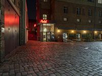 an alley with cobblestones is lit up at night and empty tables sit in the front