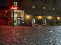 an alley with cobblestones is lit up at night and empty tables sit in the front