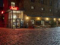 an alley with cobblestones is lit up at night and empty tables sit in the front