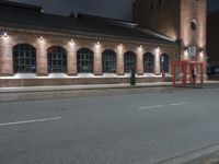 an empty road in front of brick building at night time with lit sign and light posts