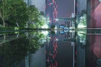 a reflection of a very tall skyscraper is in the water at night with a red light streaking through