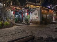 a narrow street at night with a building that has lanterns on it's side