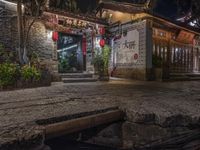 a narrow street at night with a building that has lanterns on it's side