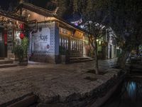 a narrow street at night with a building that has lanterns on it's side