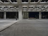 large open walkway leading up to a parking structure at night with lots of square tiles and poles at the bottom