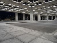 large open walkway leading up to a parking structure at night with lots of square tiles and poles at the bottom