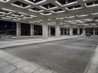 large open walkway leading up to a parking structure at night with lots of square tiles and poles at the bottom