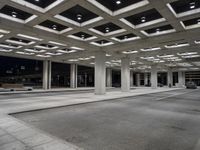 large open walkway leading up to a parking structure at night with lots of square tiles and poles at the bottom