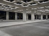 large open walkway leading up to a parking structure at night with lots of square tiles and poles at the bottom