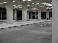 large open walkway leading up to a parking structure at night with lots of square tiles and poles at the bottom