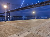 night view of a city and bridge from the ground by water, with benches around it