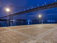 night view of a city and bridge from the ground by water, with benches around it