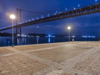 night view of a city and bridge from the ground by water, with benches around it