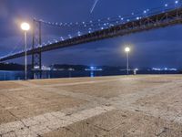 night view of a city and bridge from the ground by water, with benches around it