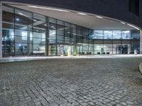 a building with many glass windows and an outside walkway at night, with a bench outside