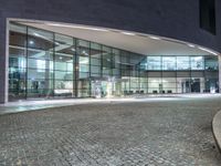 a building with many glass windows and an outside walkway at night, with a bench outside