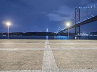 a large bridge over the ocean with street lights on it at night with bright lights on the ground