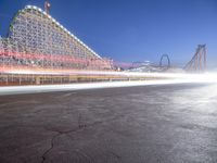 an empty parking lot near a roller coaster at night time, with long exposure of light coming from cars