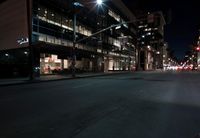 a view from the front seat of a car on a city street at night with lights shining and buildings in the background