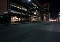a view from the front seat of a car on a city street at night with lights shining and buildings in the background