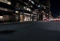 a view from the front seat of a car on a city street at night with lights shining and buildings in the background