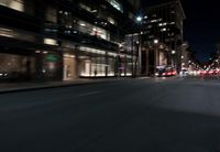 a view from the front seat of a car on a city street at night with lights shining and buildings in the background