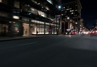 a view from the front seat of a car on a city street at night with lights shining and buildings in the background
