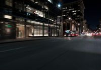 a view from the front seat of a car on a city street at night with lights shining and buildings in the background
