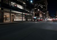 a view from the front seat of a car on a city street at night with lights shining and buildings in the background