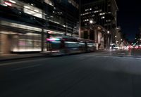 a view from the front seat of a car on a city street at night with lights shining and buildings in the background