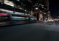 a view from the front seat of a car on a city street at night with lights shining and buildings in the background