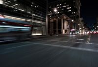 a view from the front seat of a car on a city street at night with lights shining and buildings in the background