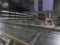 the view from atop of a pedestrian walkway of traffic and buildings at night with cars passing on the street